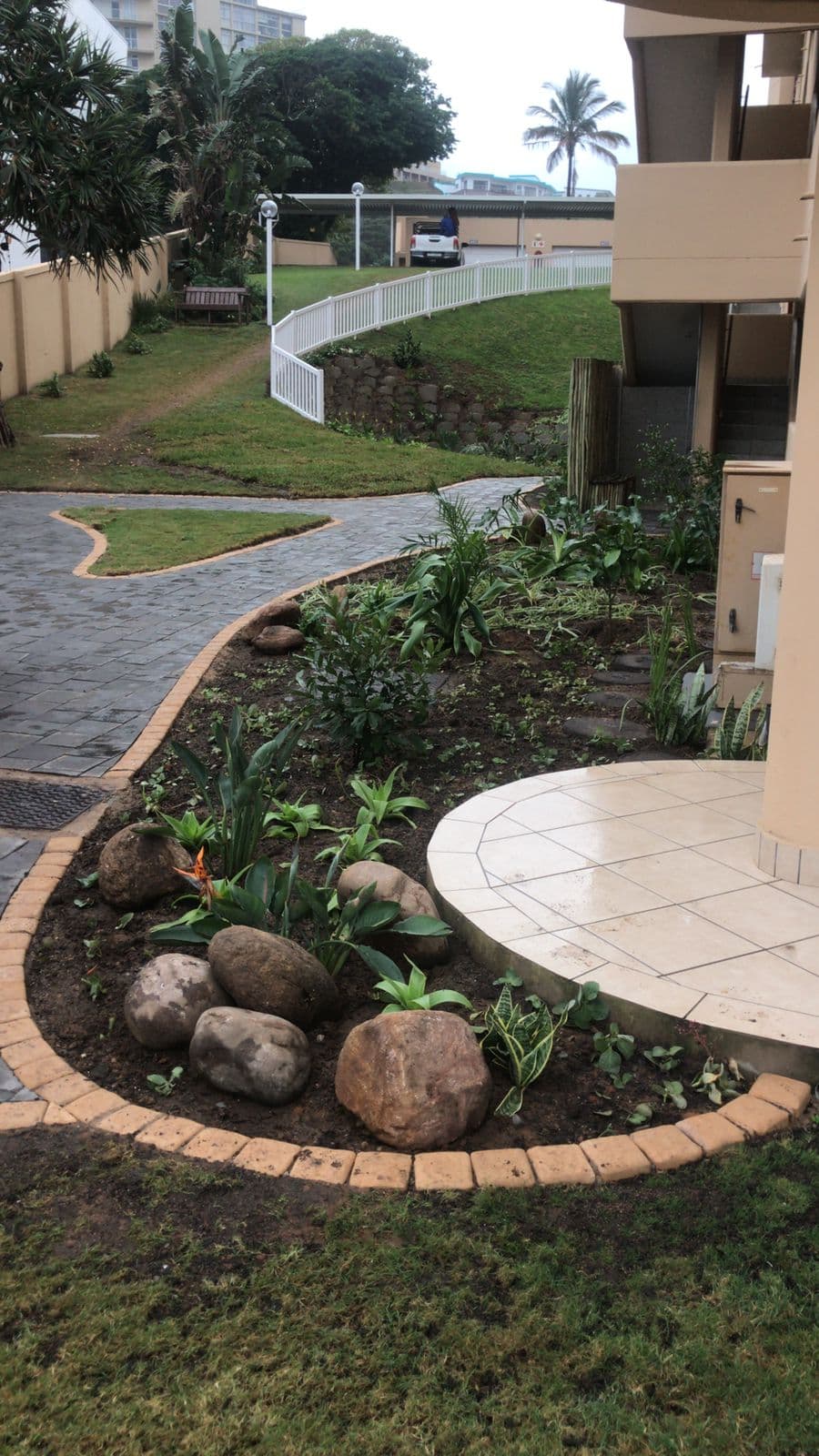 Curved garden bed with rocks and new plantings alongside paved pathway at coastal property